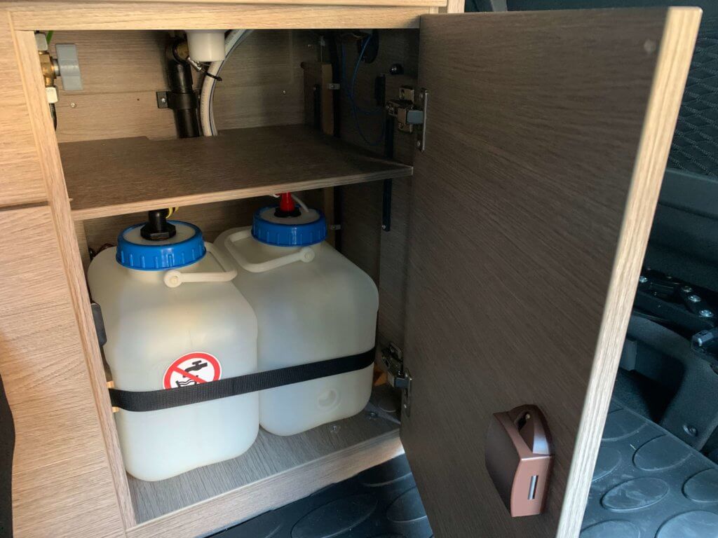 Geöffneter Schrank im Küchenmodul. Wasser und Abwasserkanister